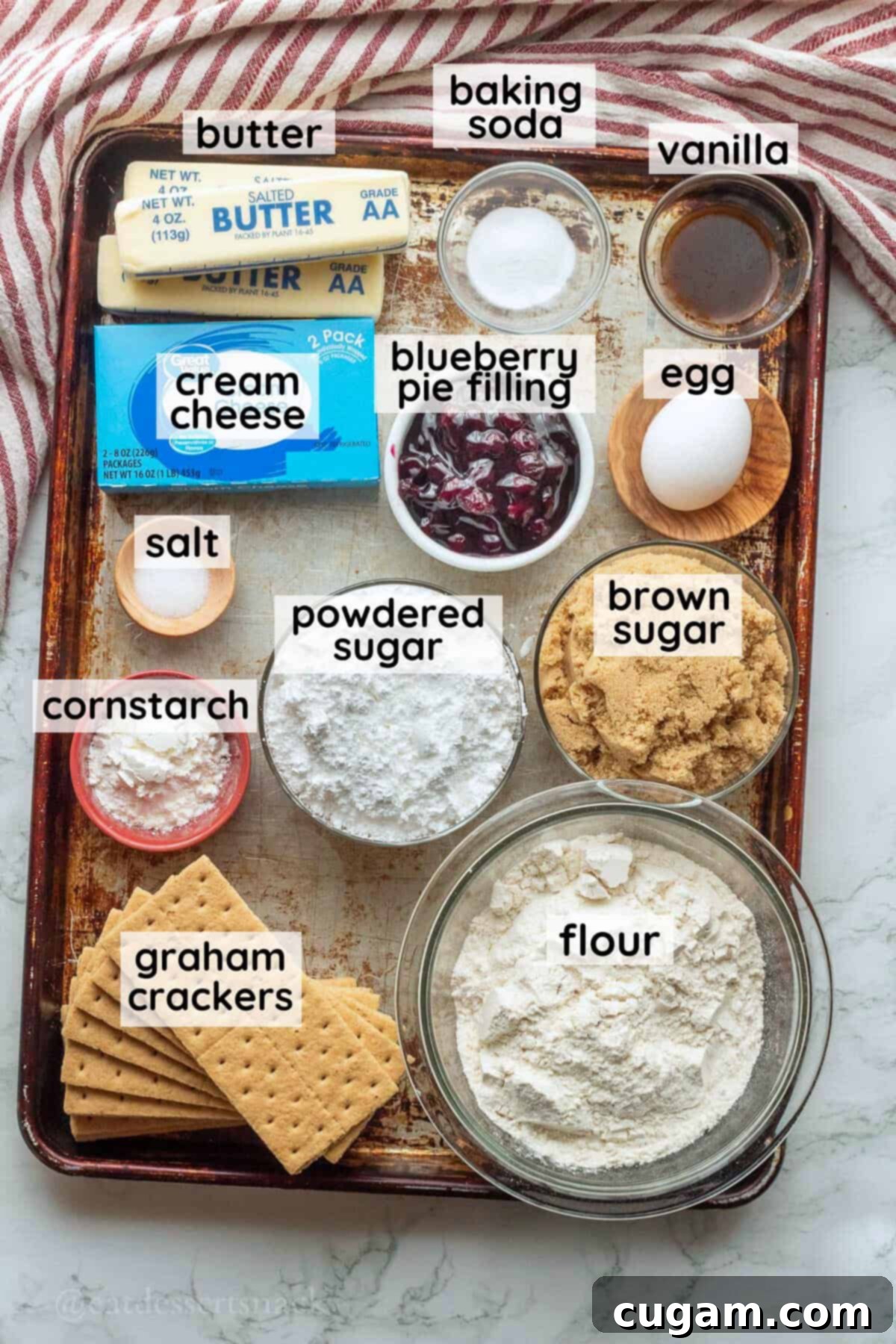 Labeled ingredients for blueberry cheesecake cookies on metal baking pan.