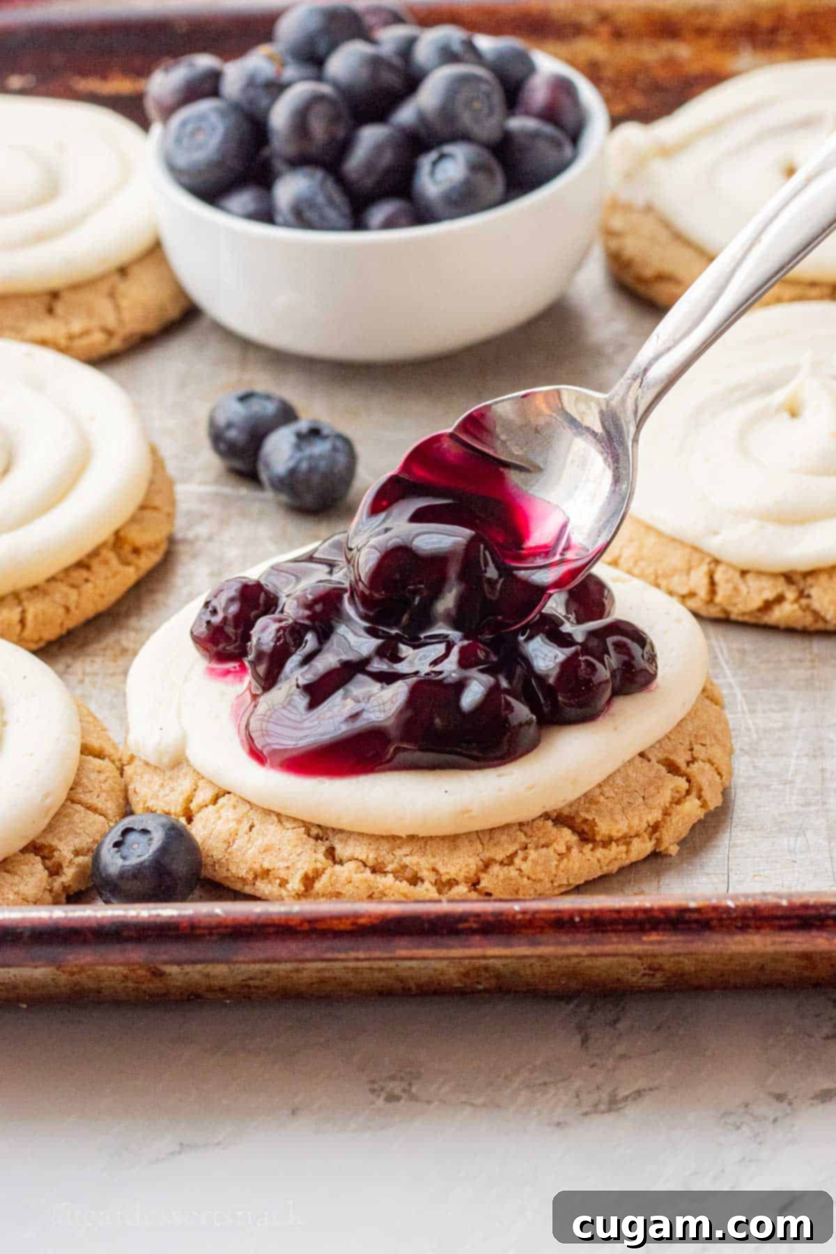 Spooning blueberry pie filling onto cheesecake cookie.