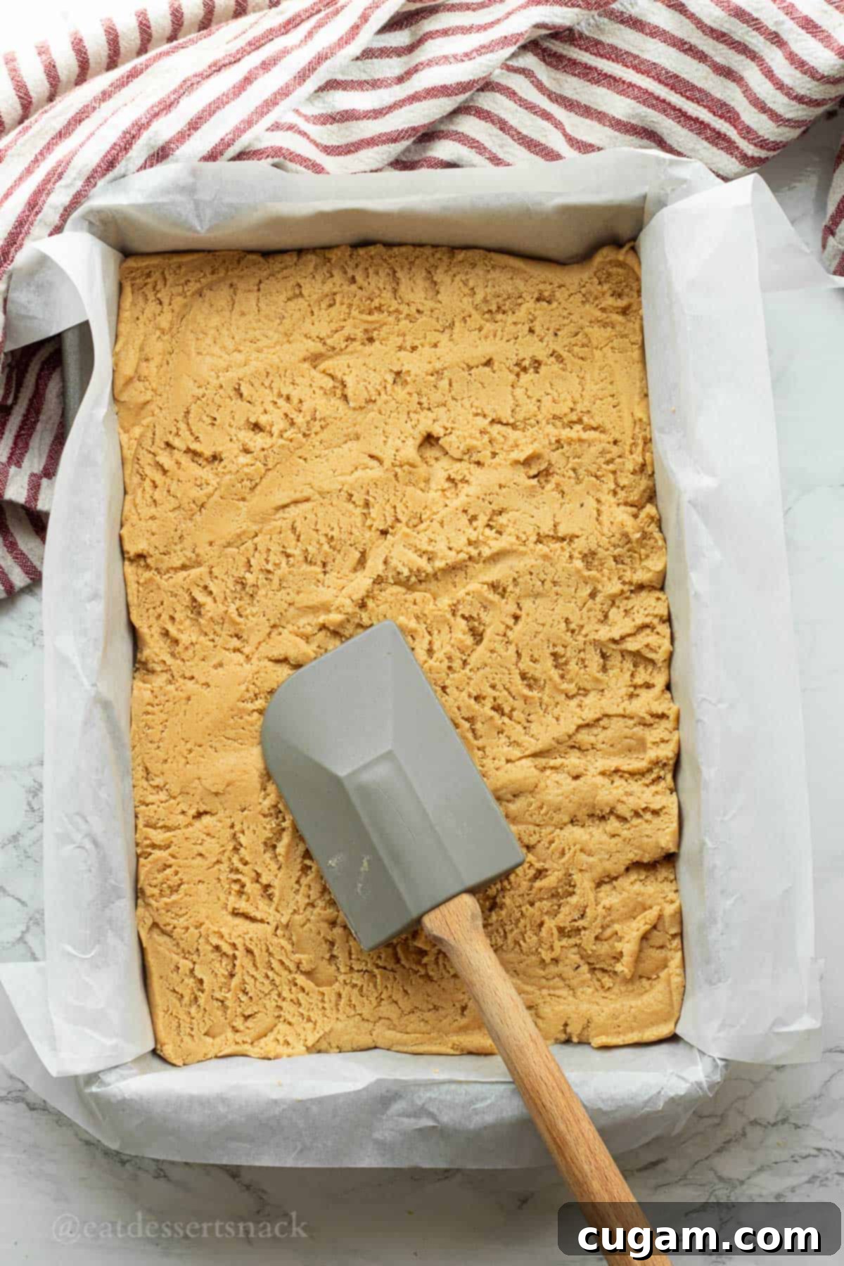 Spatula spreading peanut butter cookie batter into pan.