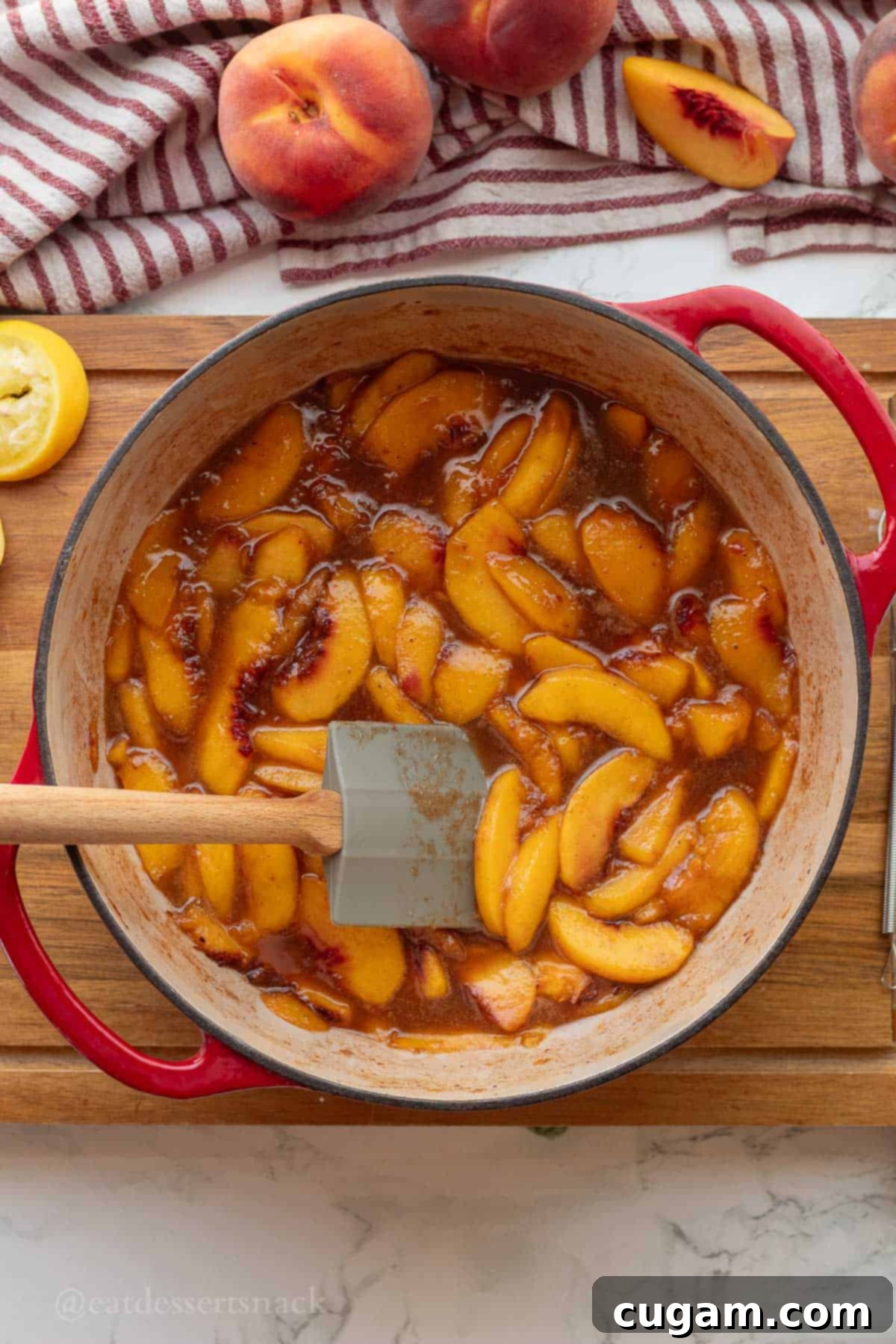 Cooked peach pie filling in a pot with a rubber spatula, showing the thick, glossy texture.