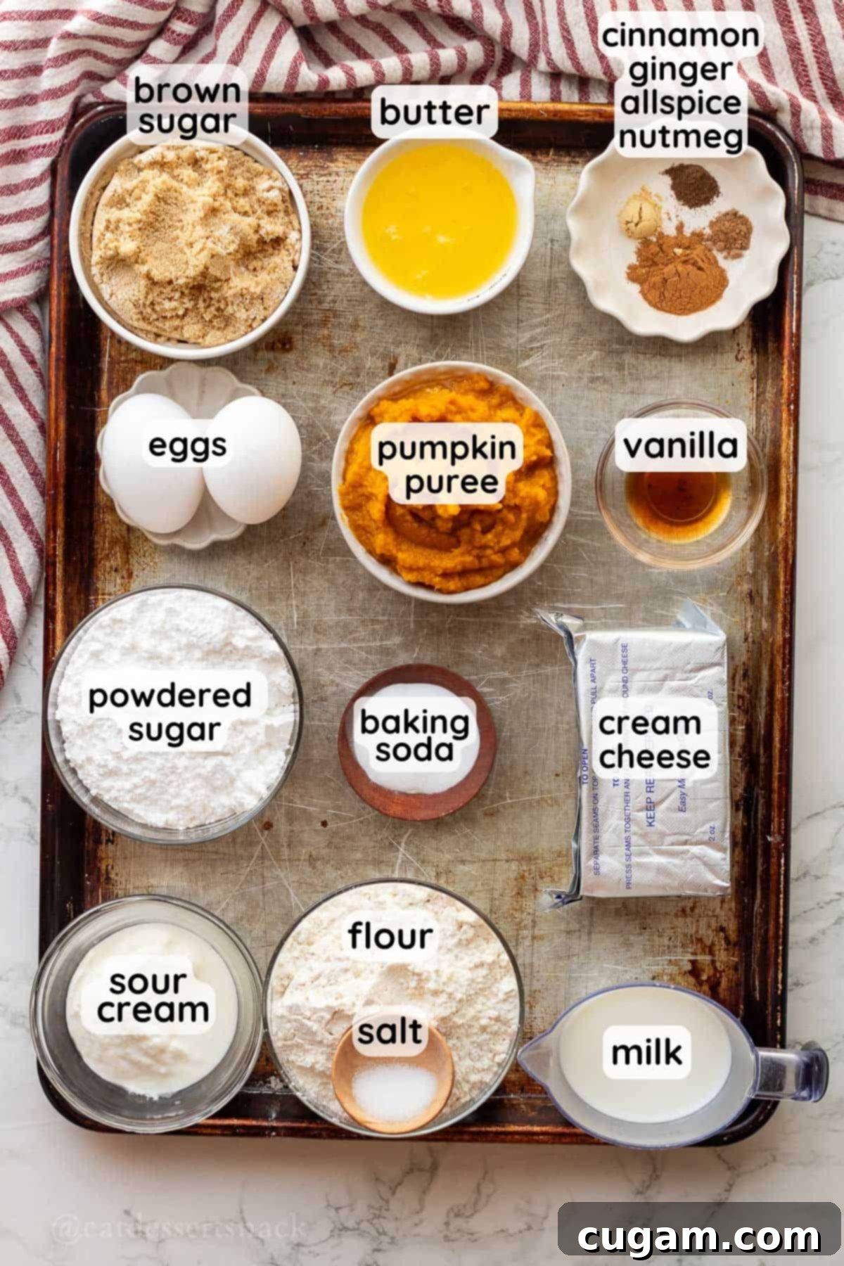 Labeled ingredients for pumpkin bread with cream cheese frosting in glass bowls on metal pan.