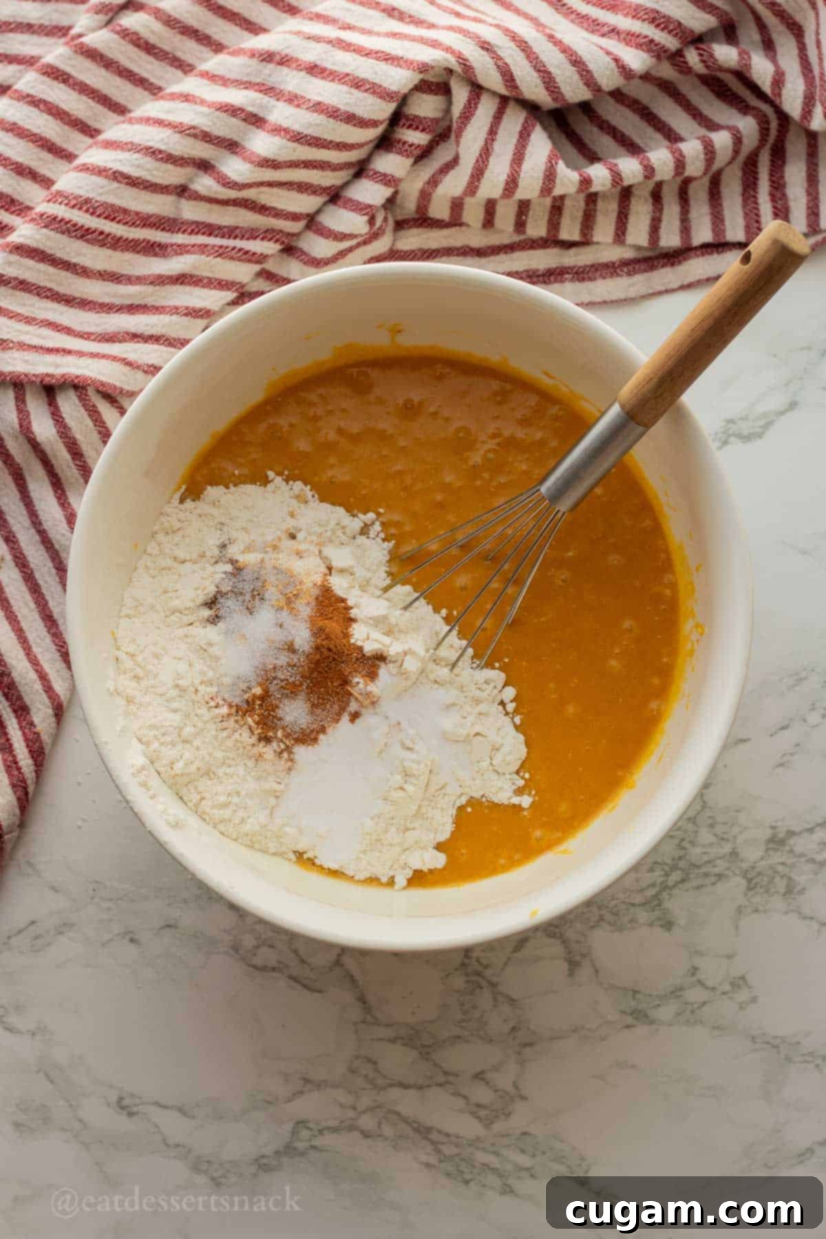 Flour and spices on top of pumpkin and wet ingredients in mixing bowl with whisk.