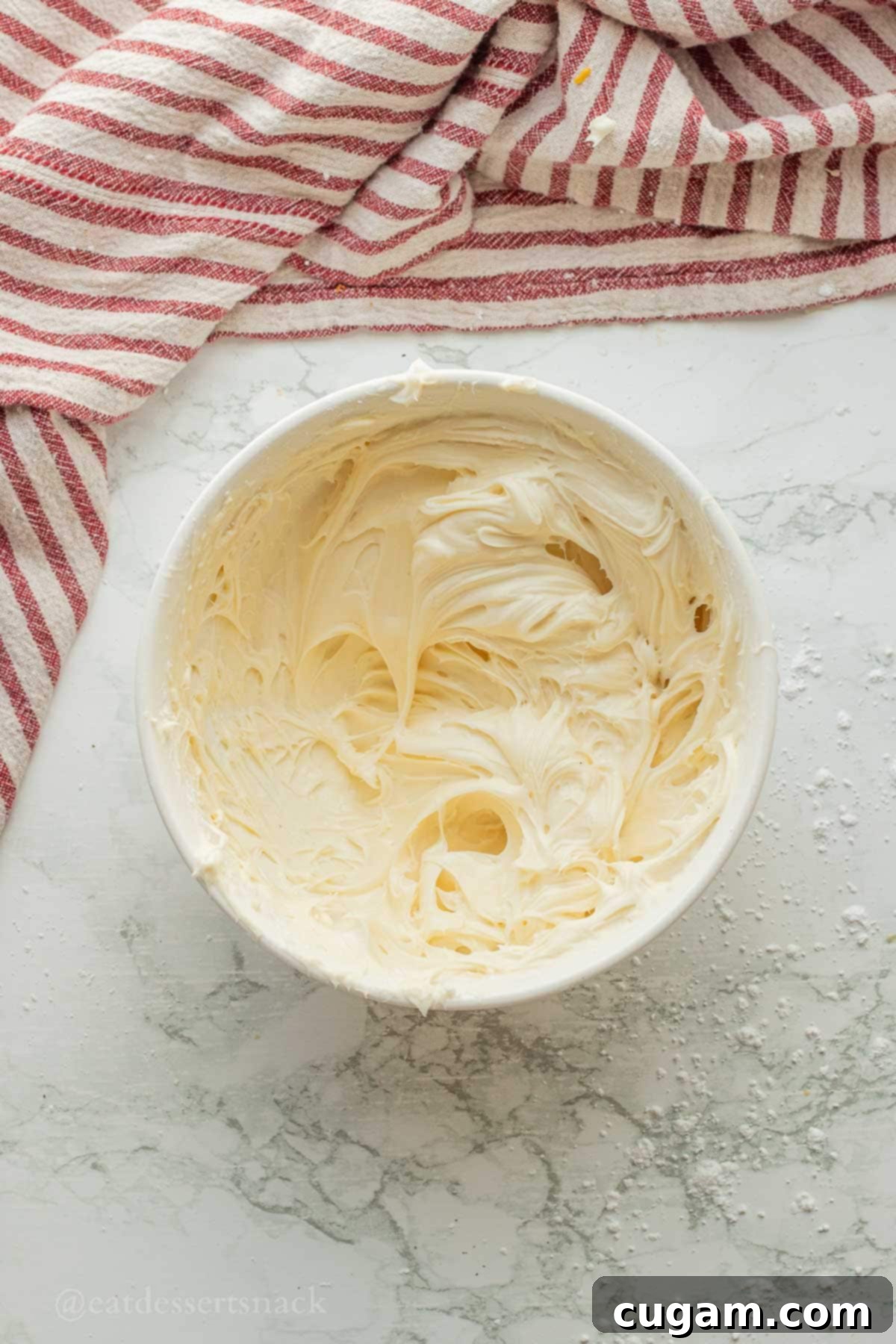Cream cheese frosting mixed into bowl with spatula.