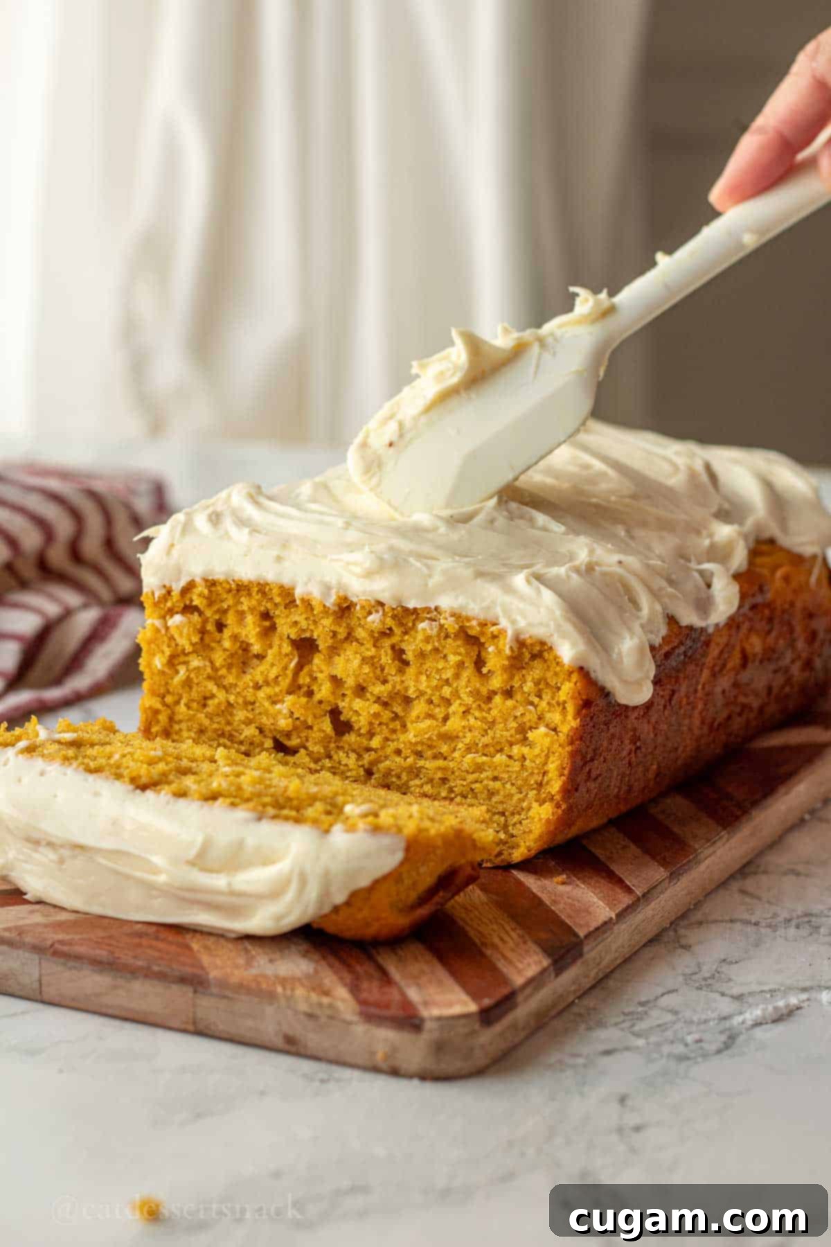 Spatula spreading cream cheese frosting on pumpkin bread.