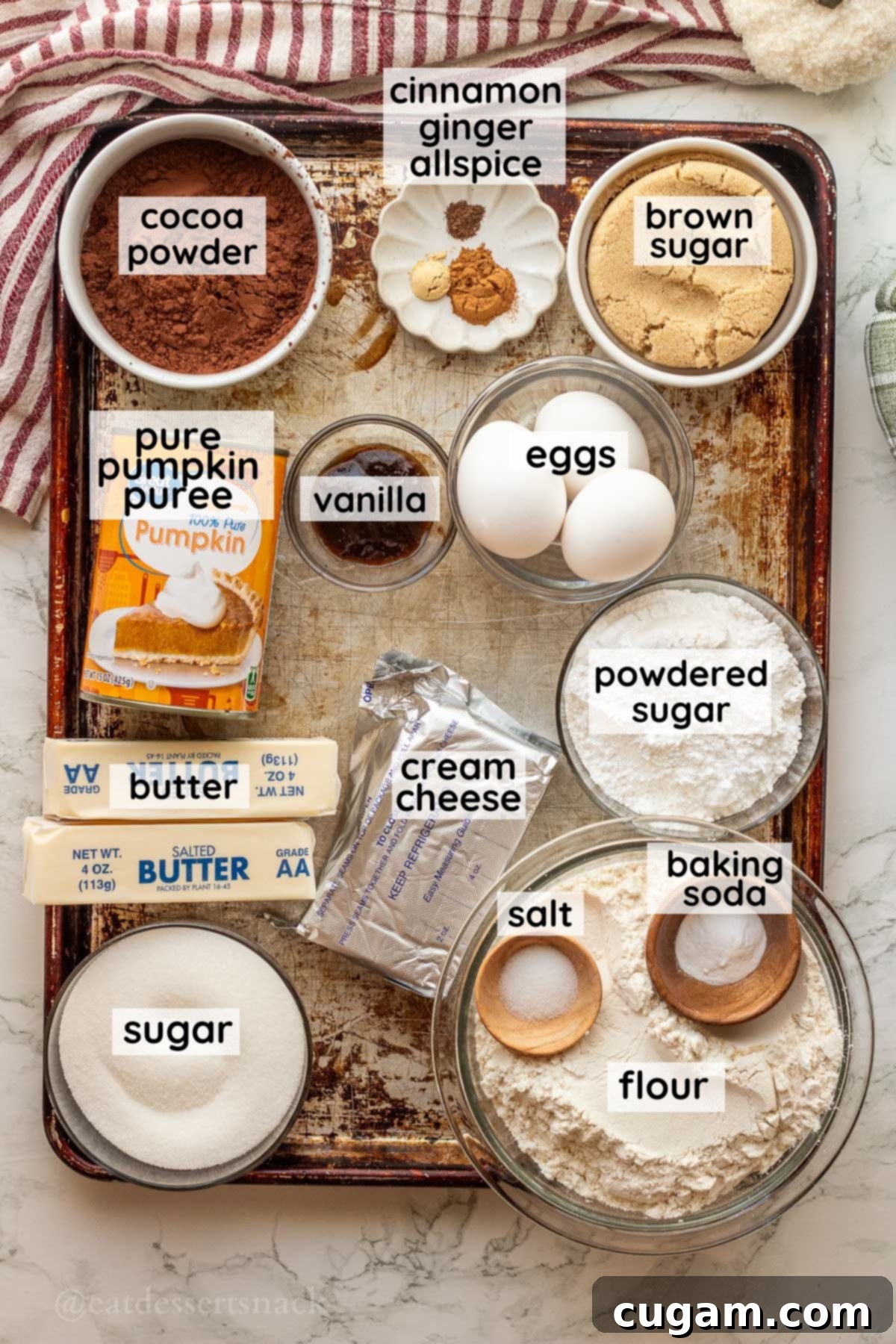 Labeled ingredients for pumpkin cheesecake brownies in glass bowls on metal pan.