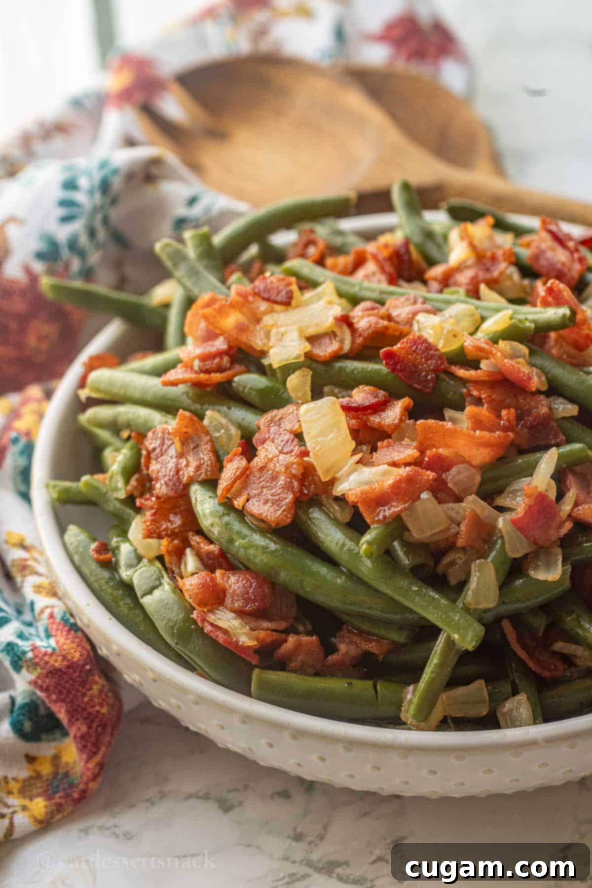 Bowl of cooked green beans with crispy bacon and cooked onions.