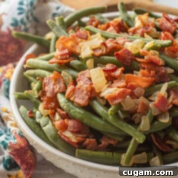 Bowl of cooked green beans with crispy bacon and cooked onions.