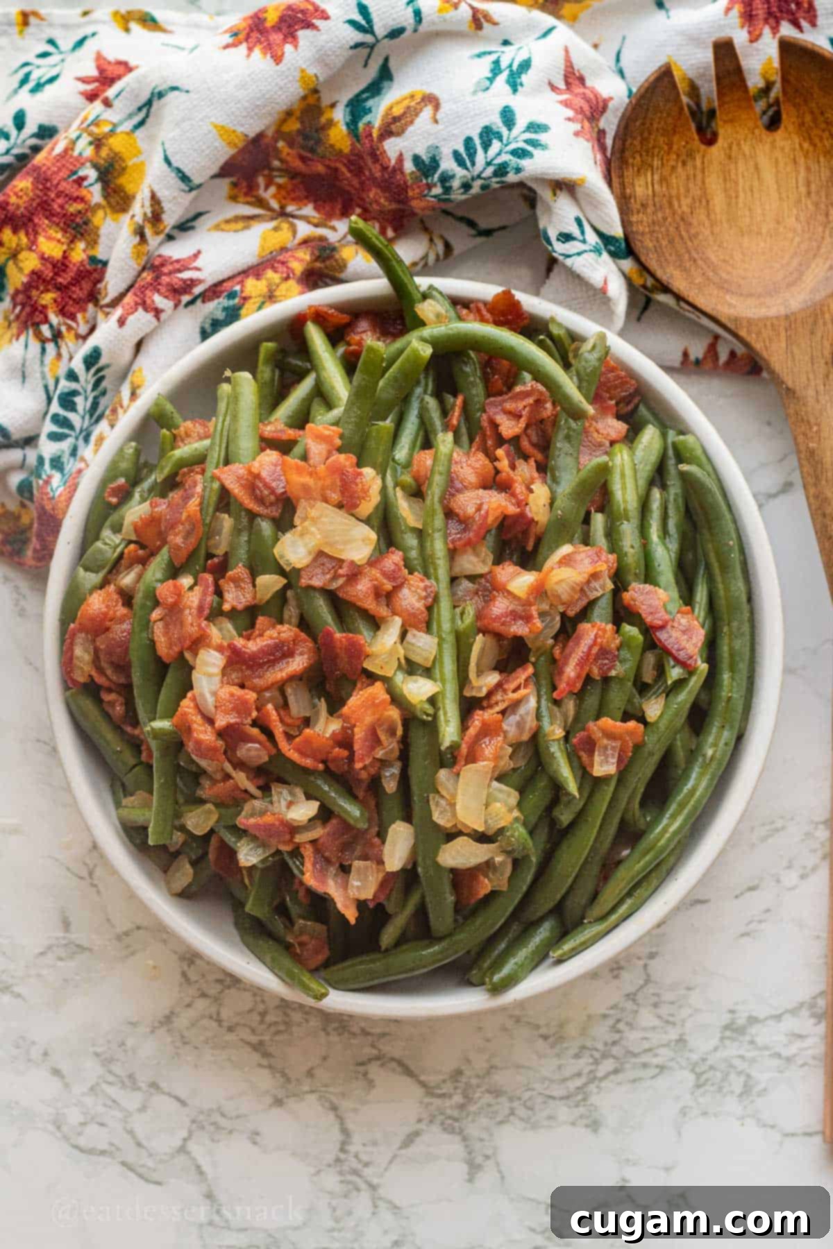 Bacon and onion on bowl of cooked green beans with wooden spoon.