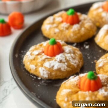 Baked pumpkin sugar cookies on plate, featuring their crinkled tops and candy pumpkin centers.