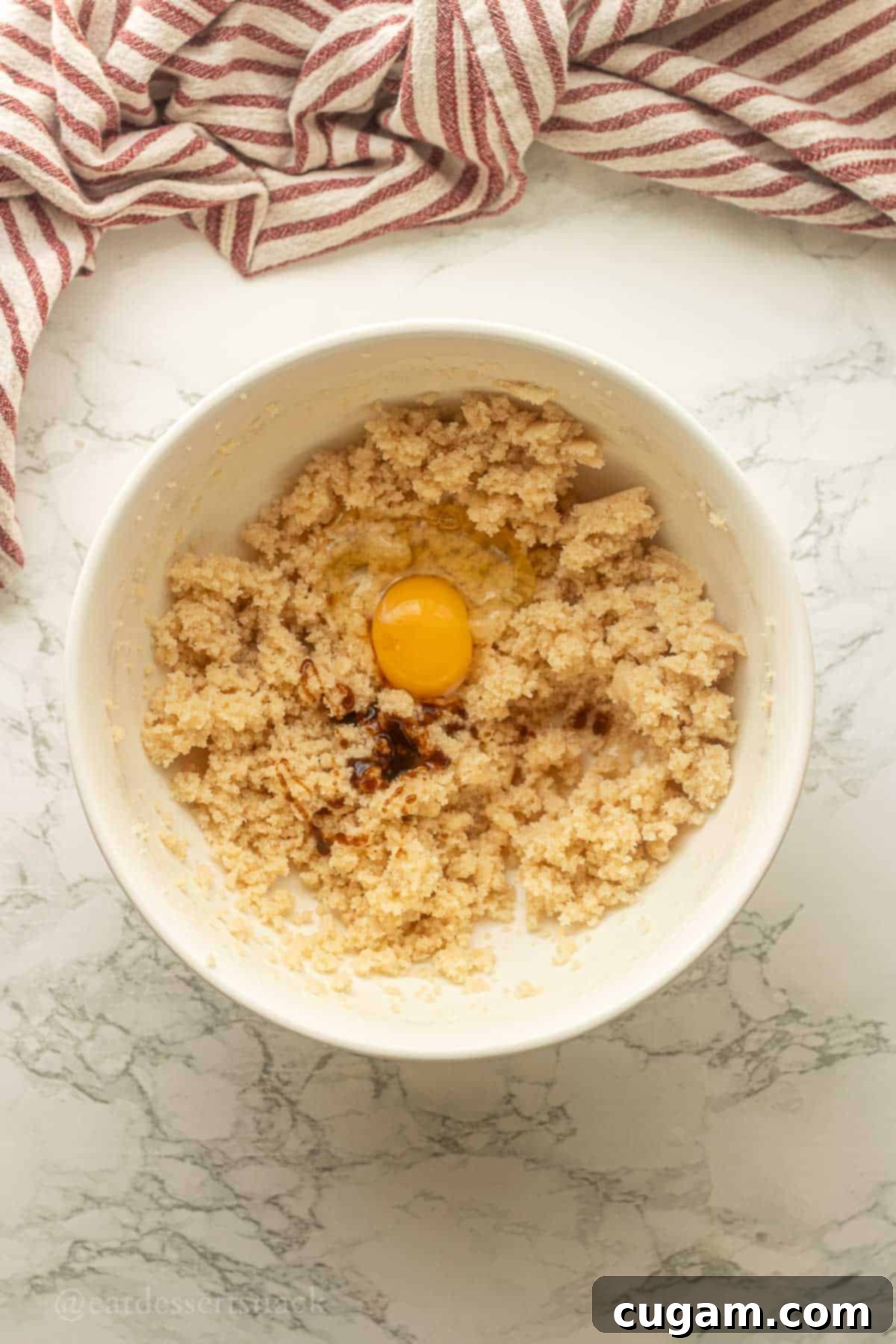 Egg and vanilla in bowl of creamed sugar and butter, ready for mixing.