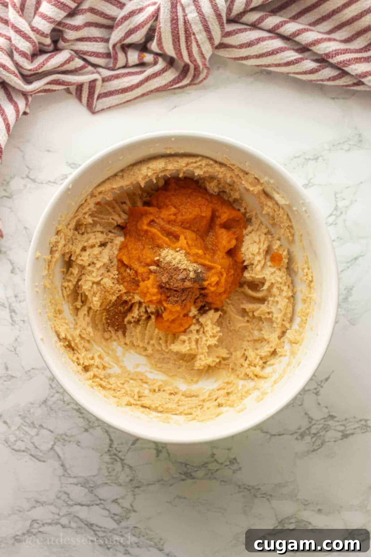 Pumpkin puree and pumpkin spice in bowl of creamed butter and sugar, ready to be incorporated.