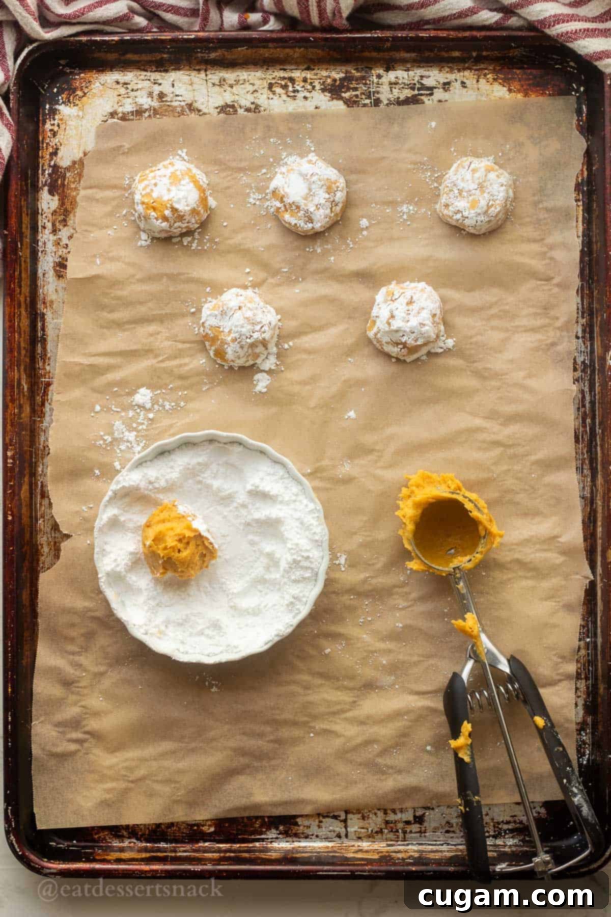 Powdered sugar on rolled raw pumpkin cookie dough balls, ready for baking.