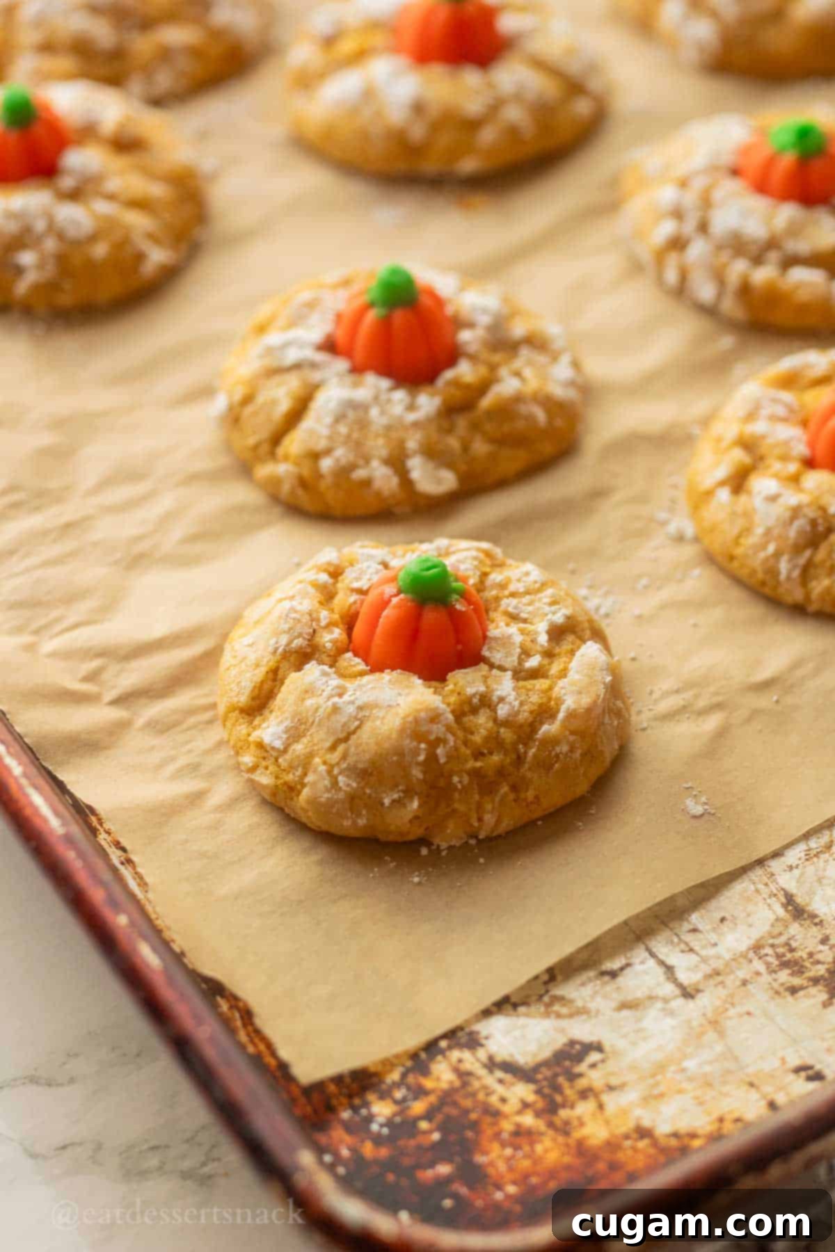 Baked pumpkin sugar cookies on parchment paper on metal pan, with candy pumpkins in the center.