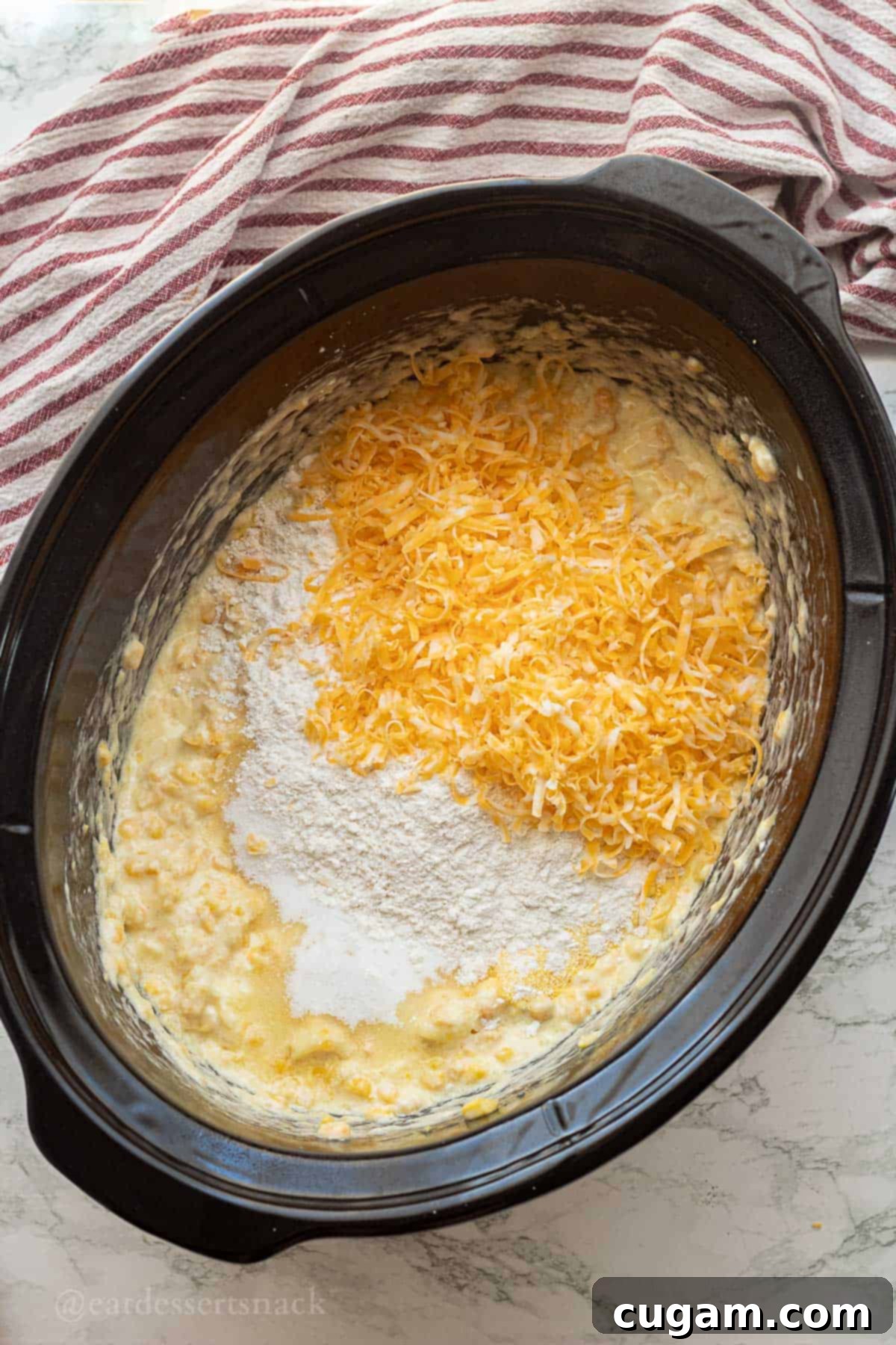 Raw corn pudding batter with cheese in slow cooker.