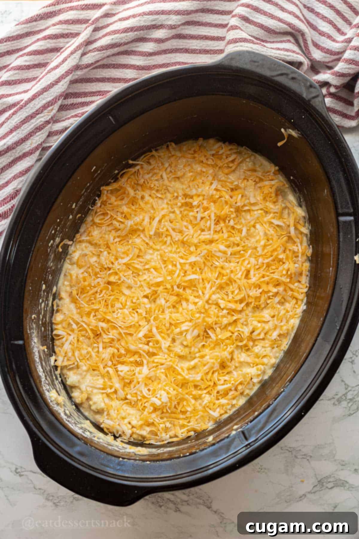 Shredded cheese on top of raw corn pudding batter in slow cooker.