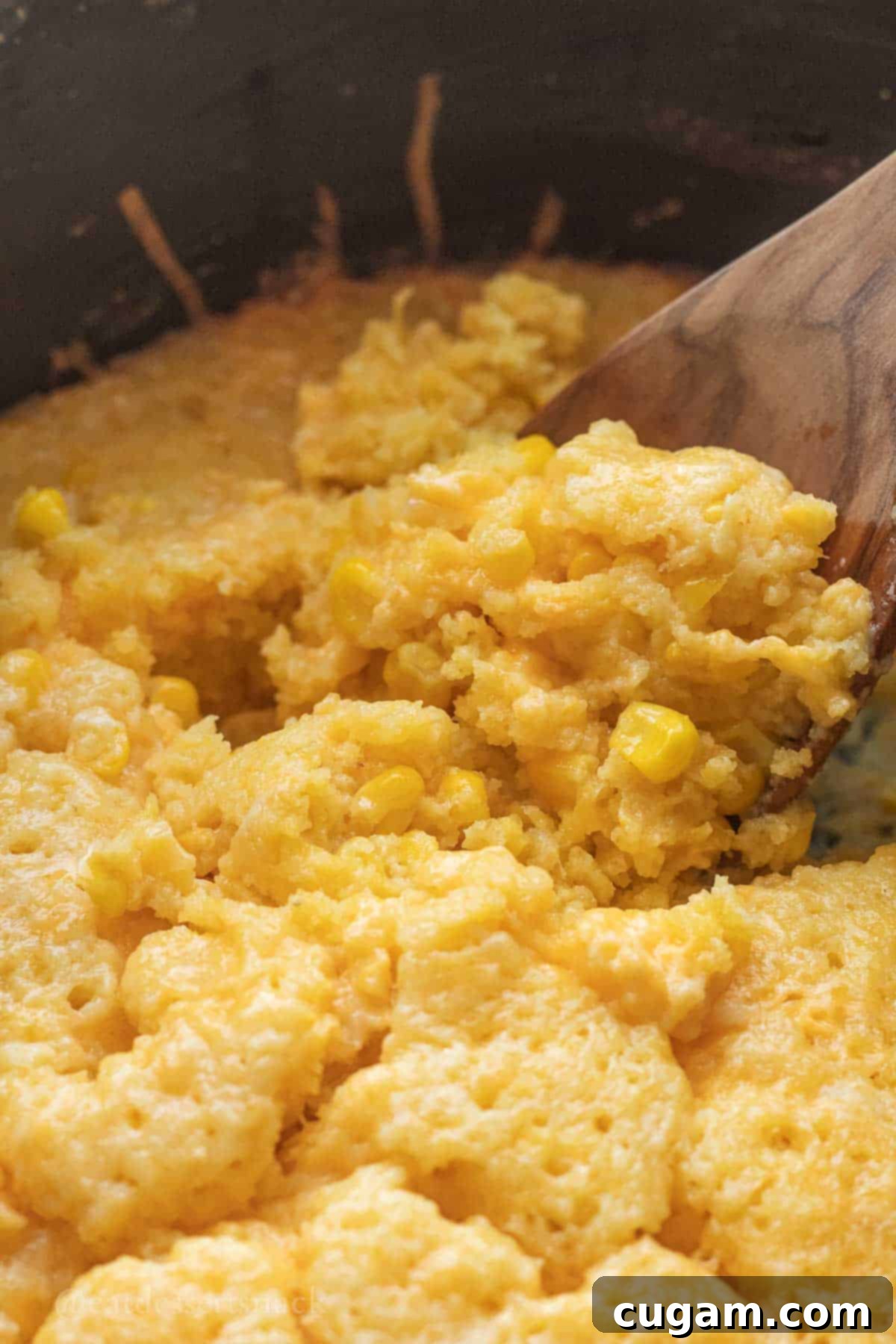 Cooked cornbread pudding in slow cooker on spoon.