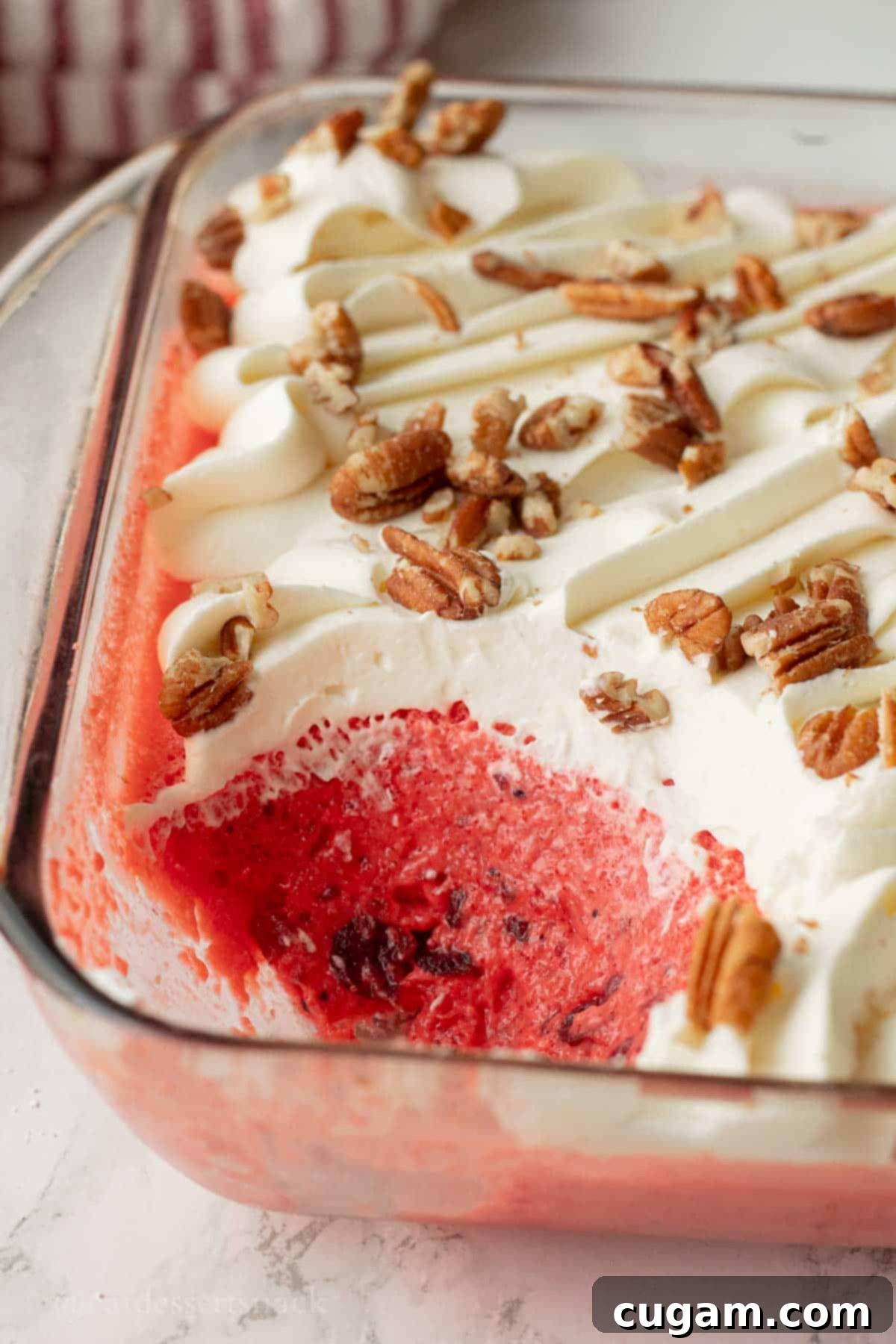 A serving spoon lifting a creamy, pink cranberry Jello salad portion from a clear glass dish, highlighting the smooth texture and bits of whole cranberries.