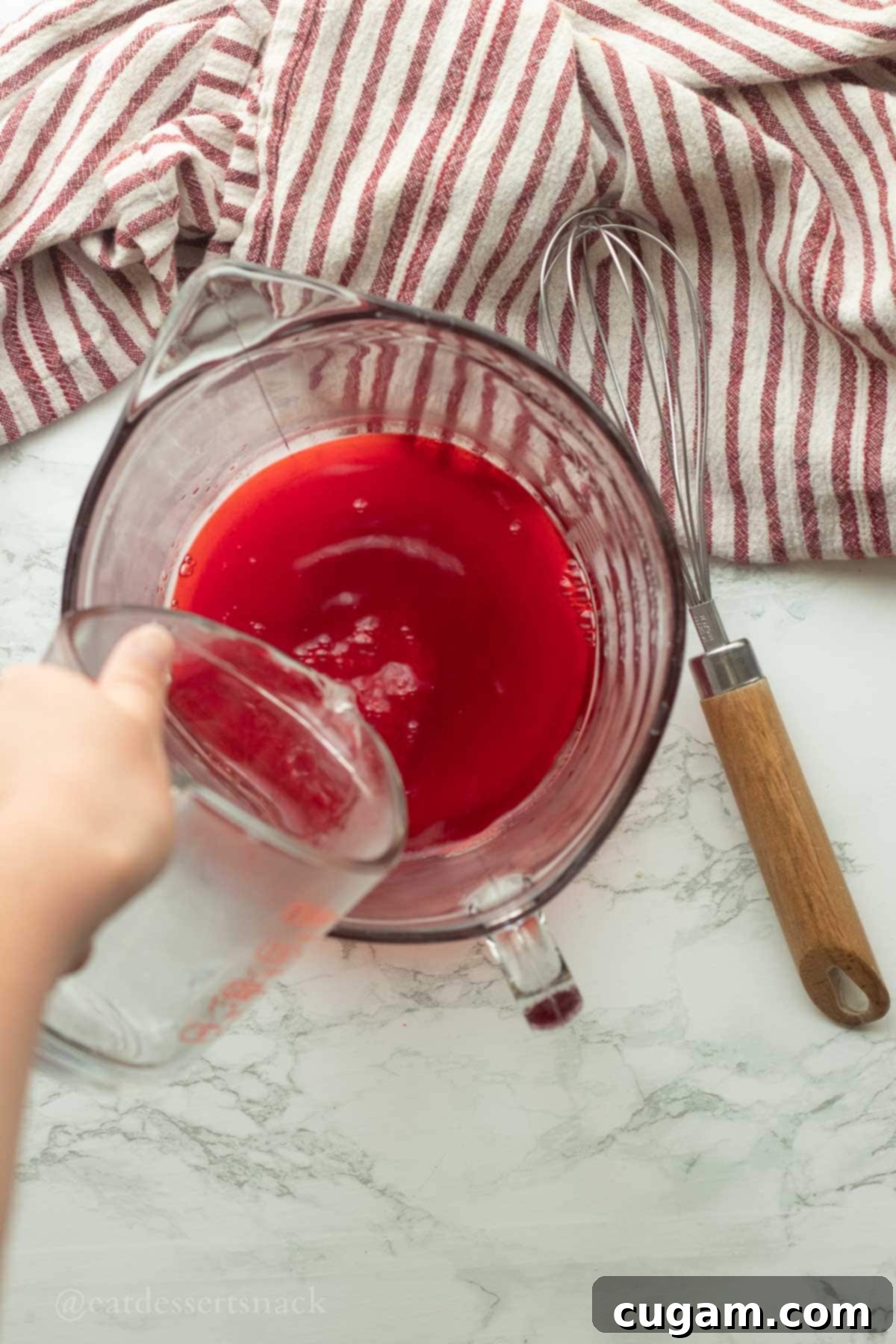 Boiling water being poured into a bowl containing raspberry jello powder, ready to be whisked for the base of the jello salad.