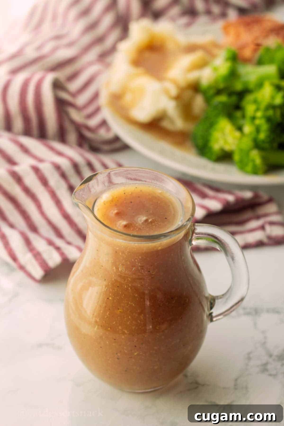 A glass pitcher of perfectly smooth brown gravy displayed on a marble surface, showcasing its rich color and texture.