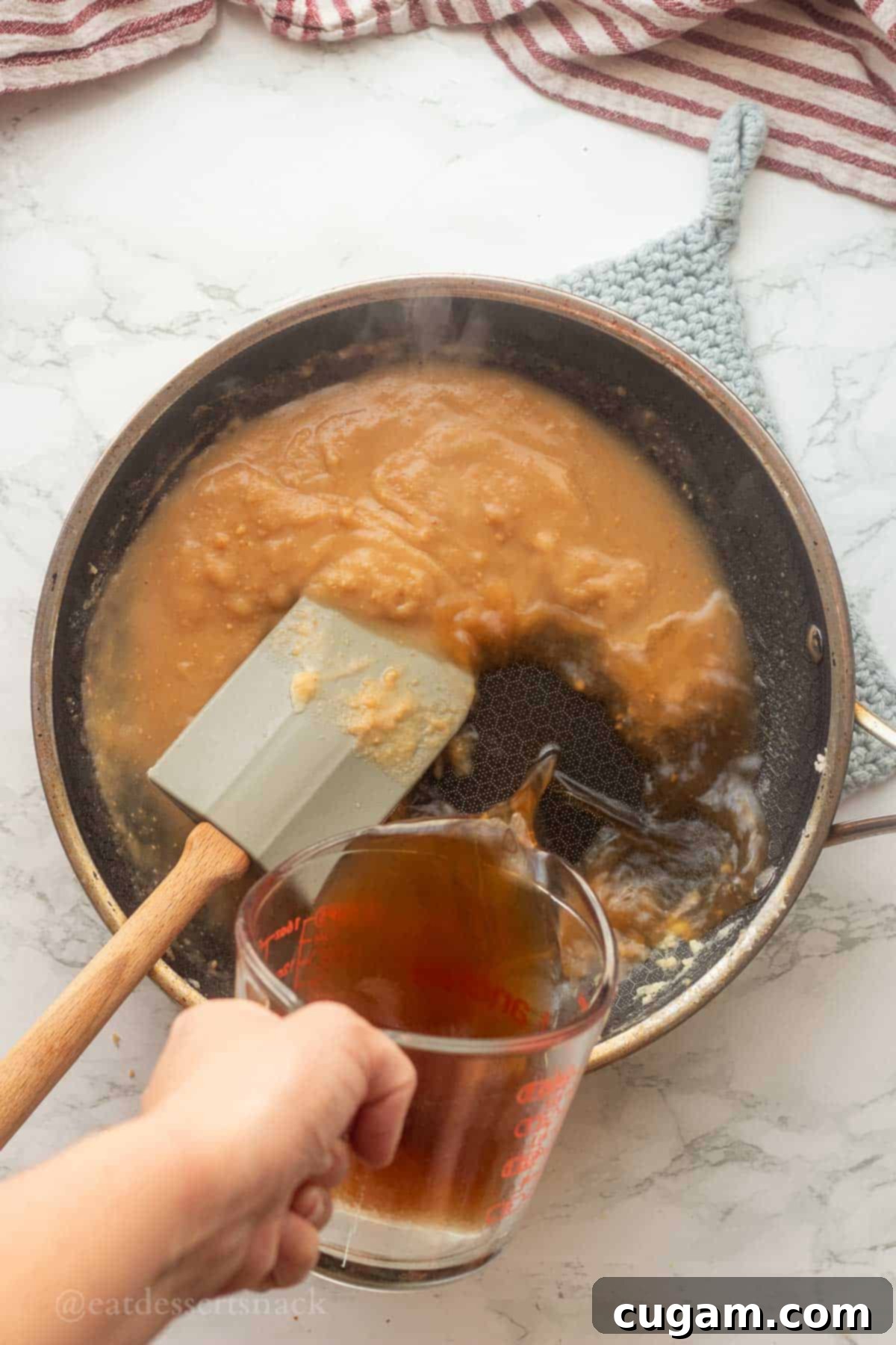 A hand pouring warm broth into a pan of prepared roux, demonstrating the gradual incorporation of liquid for a smooth gravy.