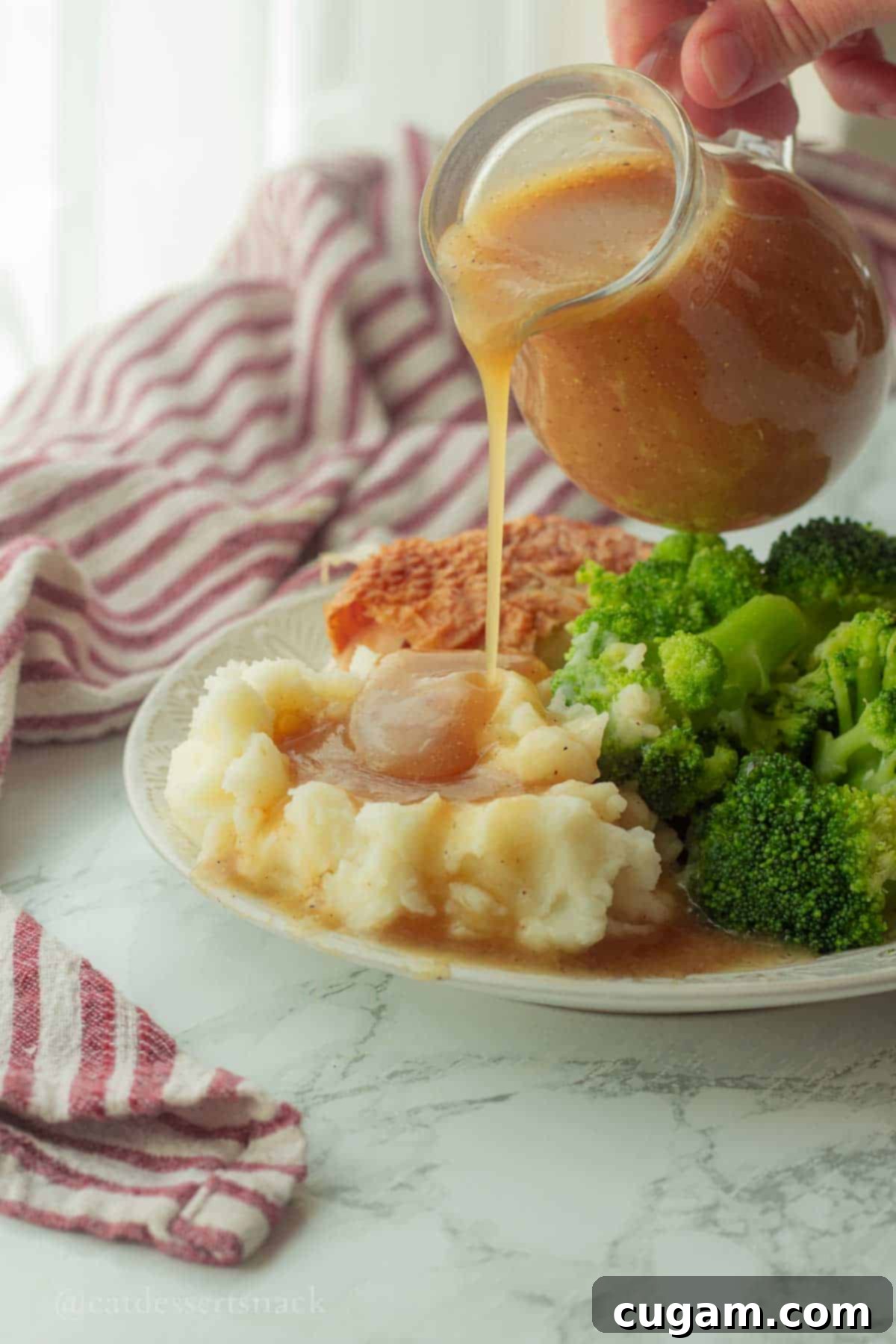 A close-up of delicious brown gravy being poured generously onto a plate of potatoes, creating a mouthwatering visual.