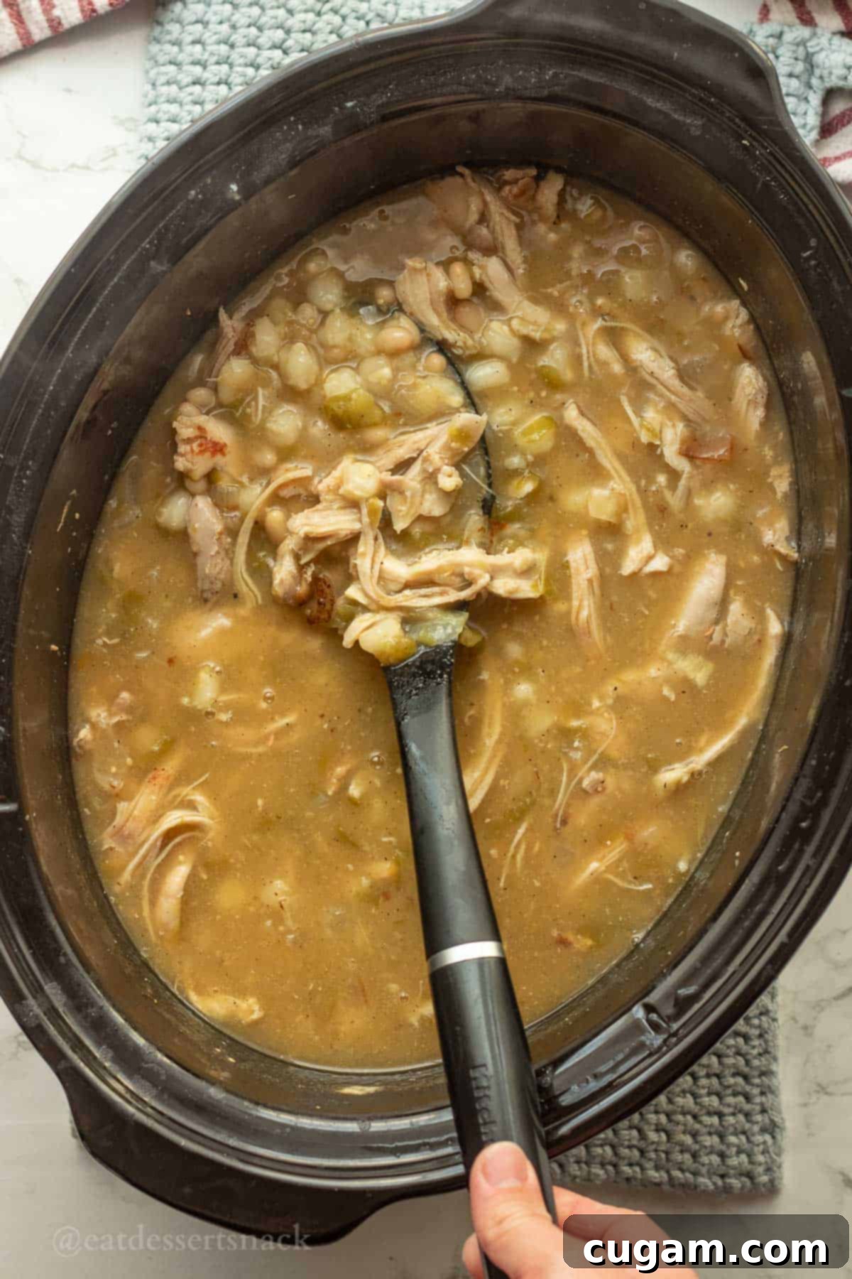 Green Chile Chicken Stew 8 Shredded chicken in crockpot of posole with serving spoon.