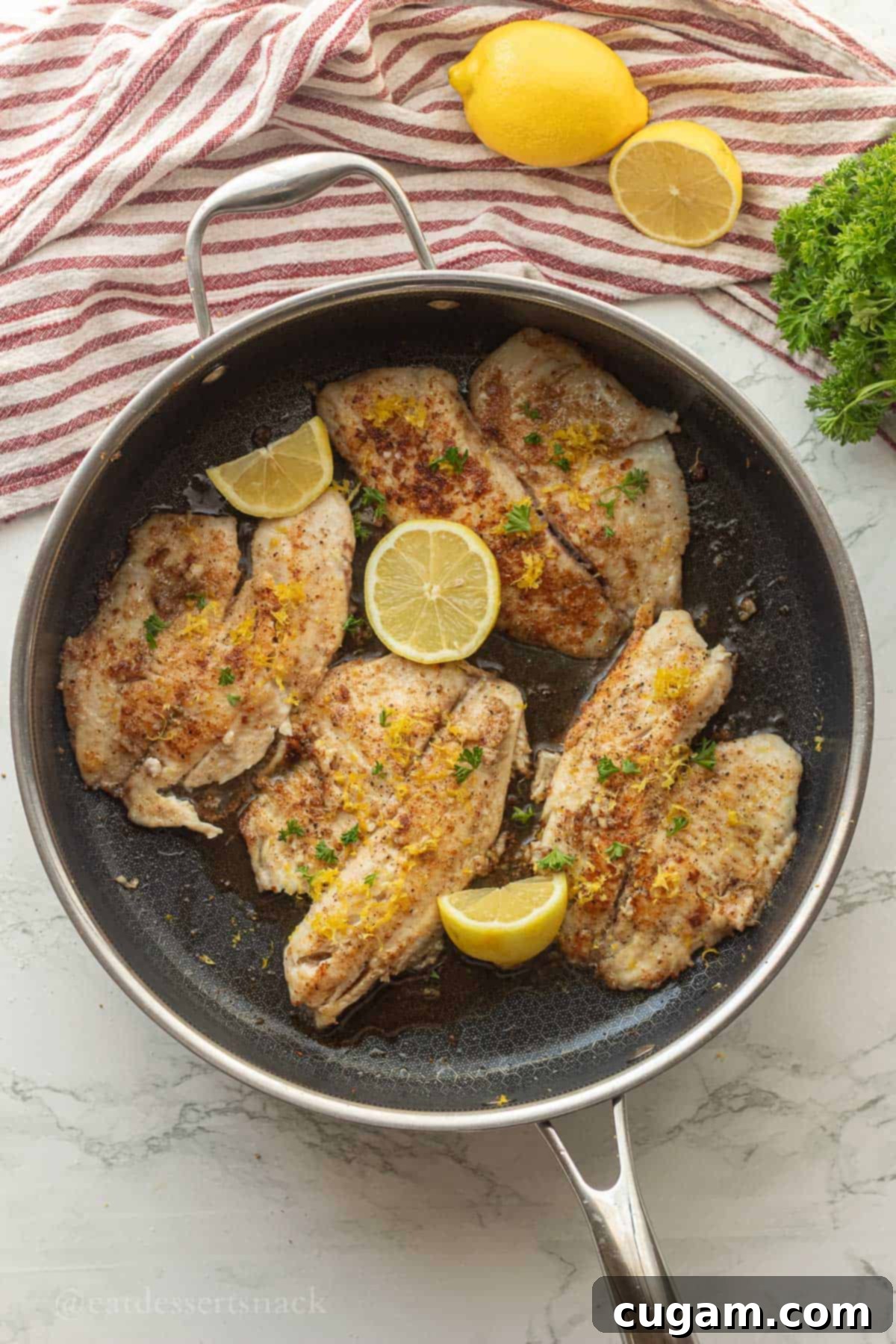 Perfectly Zesty Lemon Pepper Tilapia 7 Four tilapia fillets cooked in a pan, garnished with lemon slices and parsley.