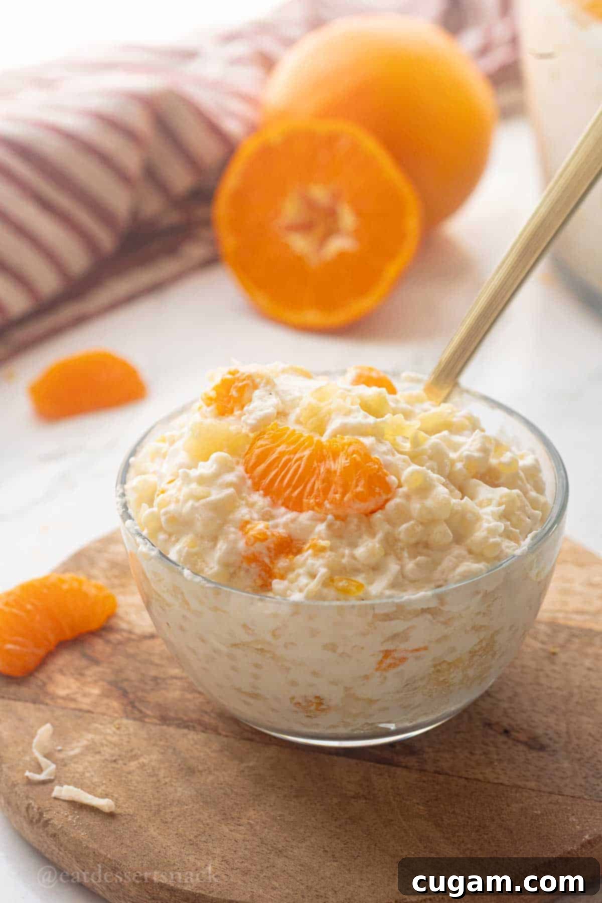 Frog Eye Salad 2 Glass bowl of frog eye salad with gold spoon on wood cutting board.